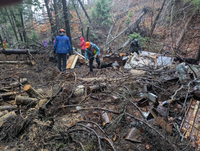 Two people work in a wooded section clearing logs from the forest floor to improve a walking trail.